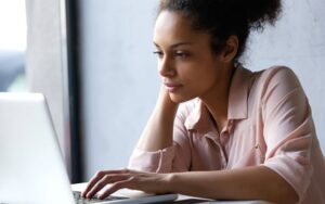 A woman in a pink shirt works on a laptop