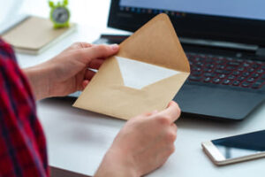 Someone opening a piece of direct mail in front of a laptop.